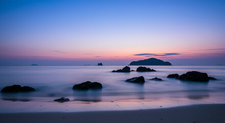 Tranquil twilight over a tropical beach with rocky shore and distant islands, long exposure
