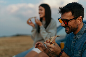 Happy couple enjoying pizza outdoors at sunset during road trip