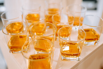 Multiple glasses of amber liquid served at event indoors on a white table