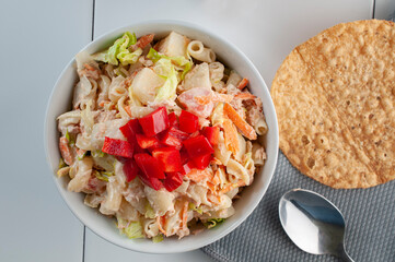 White bowl of tuna salad with mayonnaise paste and red peppers on top on a white table with a spoon and a Mexican tostada on the side. top view or flat lay image