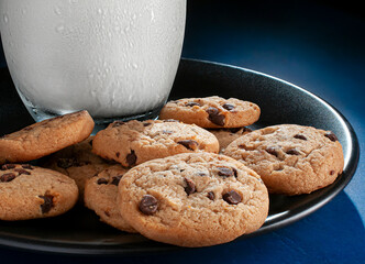 Chocolate chip cookies with a glass of cold milk on a dark plate on a blue table, foods high in carbohydrates and unhealthy sugars macro photography  horizontal image