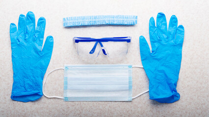 Medical face mask, glasses, hat and gloves laying on table flat lay view with copy-space