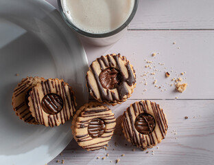 Vanilla cookies filled and covered with chocolate on a white plate and on a white wooden table, foods high in sugars and carbohydrates top view 