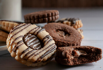 Macro photography of vanilla and chocolate cookies filled with chocolate with a blurred glass of milk in the background, concept of foods high in carbohydrates with a bitten cookie in the forehground