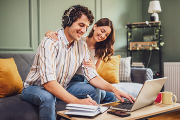 Obraz premium A man and woman sit together at home, checking their shopping list while using a laptop. Their collaborative effort highlights the organized approach to online shopping.