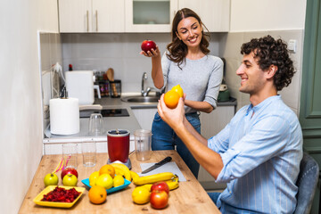 A happy young couple making a fruit smoothie together at home using a blender, enjoying healthy eating and domestic life.
