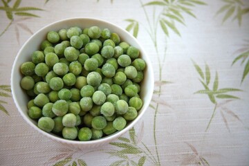 Close-up of frozen green peas in a white bowl placed on a table with copy space, healthy vegetable concept.