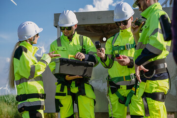 Maintenance engineer team standing at windmills at wind turbine farm. Group of people wear safety...