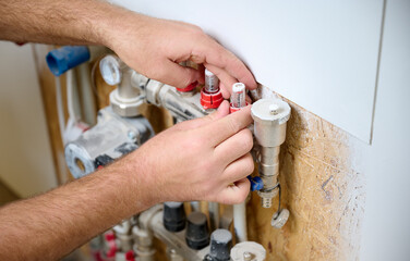 Man adjusting the heating system in a new apartment. Plumber adjusting heat on the central system valves. Service man adjusting house heating system. Underfloor heating system. Crop view