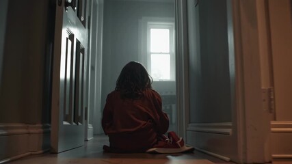 Cinematic moody corridor home, dim small child sitting floor covering face, walls, anxiety and depression dust particles floating, soft cinematic 4K ultra slow dolly dark muted high emotional tension - Powered by Adobe