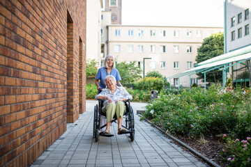 Older caregiver pushing senior woman in wheelchair.