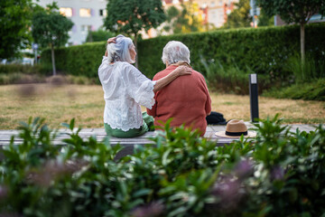 Elderly mother sitting on bench with adult daughter.