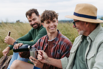 Grandfather, father and teen boy hiking togeter in nature, having cup of tea.