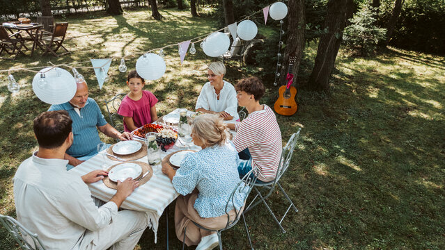 Areal view of grandparents, parents and kids dining together outside. - Powered by Adobe