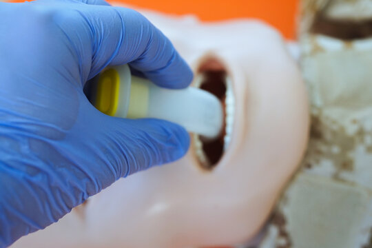 A gloved hand inserting an oropharyngeal airway tube into a medical training mannequin in camouflage uniform for airway management practice. Correct demonstration of airway tube placement during tccc.