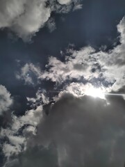 Obraz premium Dramatic skyscape with the sun's rays breaking through dark, moody storm clouds against a vibrant blue sky.