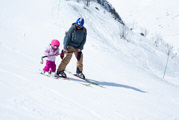 A 3-year-old girl skiing with her father on a green ski slope.