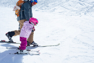 Side view of a man practising telemark skiing with his little daughter on a sunny winter day.