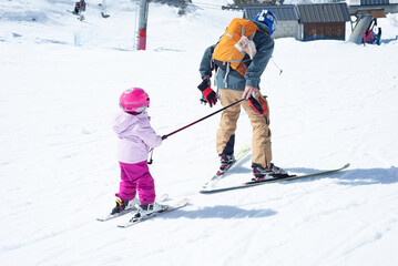 Father pulling his little daughter with his ski pole on a nice ski day.