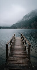 Fototapeta premium Wooden pier extends into a misty lake, mountains in the background