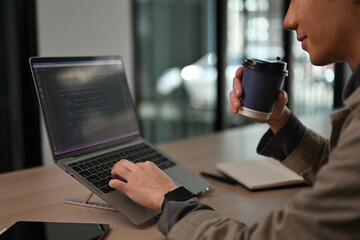 Side view and close-up of a software developer working on code with a warm drink, creating a casual yet professional workspace vibe