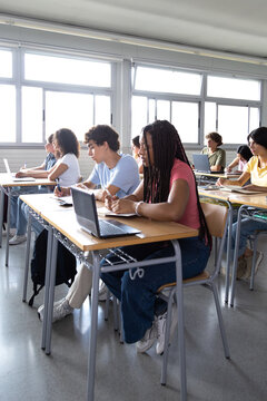 High school students studying in classroom with laptops and notebooks