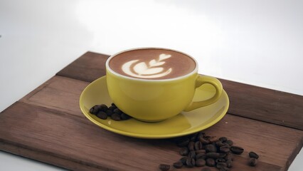 Aromatic latte art in a bright yellow cup with roasted beans on a wooden board