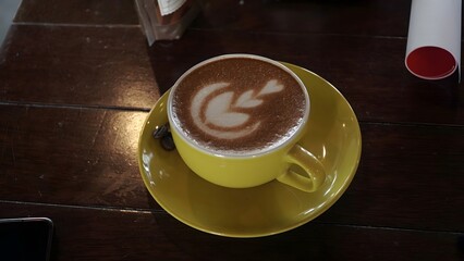 Warm and inviting latte art coffee served in a bright yellow cup on a rustic wooden table