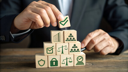 Businessman carefully stacking wooden blocks with business icons representing success strategy and legal compliance in a structured pyramid formation