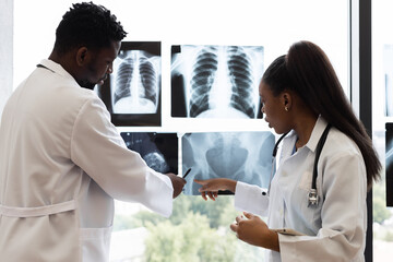 Male and female doctors analyzing x-rays together in a well-lit clinic environment near window....
