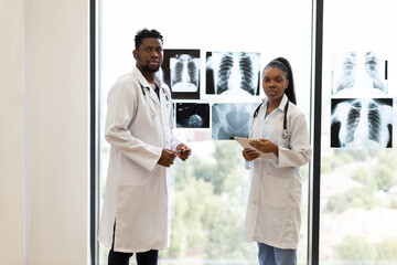 Male and female doctors evaluating x-rays in modern clinic near window, collaboration focus