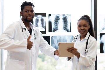Male and female doctors, adults, consulting at clinic near window analyzing x-rays displayed.