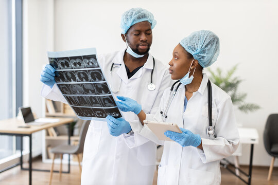 Medical professionals wearing protective gear analyzing chest x-ray scan together during consultation. Both are discussing diagnostic results in modern hospital environment.
