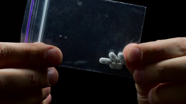 faceless man holding a bag of drugs.
LSD and methamphetamine in a transparent bag.
Drug trade and drug trafficking.
Concept of addiction and drug business