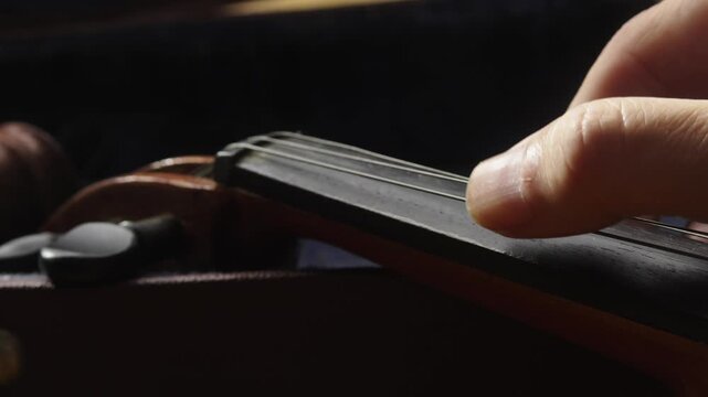 Musician thumb plucks violin strings for musical tone tuning