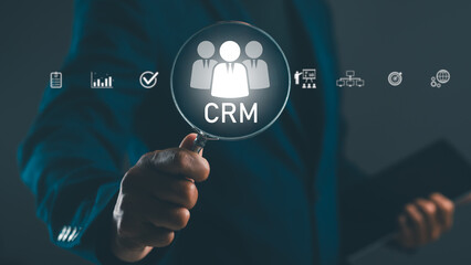 A professional hand holding a magnifying glass over a CRM icon, symbolizing customer relationship...