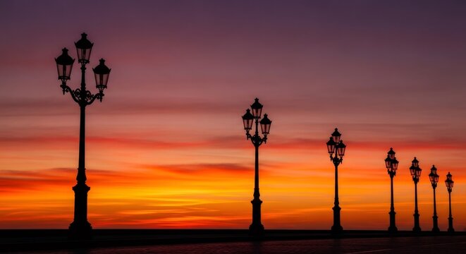 Row of street lights in silhouette against a dramatic sunset sky. Urban light system for city evening illumination concept. - Powered by Adobe