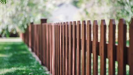 Classic wooden picket fence separating a manicured green lawn from a blurred natural background, perfect for a cozy home and garden theme