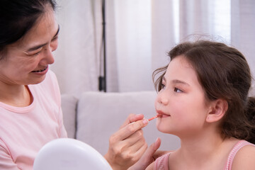 Asian mother carefully applying lipstick to daughter, loving family scene highlighting pamper and trust, routine beauty care showing confidence, bonding and gentle expression in daily lifestyle