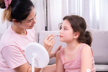 Asian single mother applying eyeshadow to daughter with smile, bonding moment during makeup...