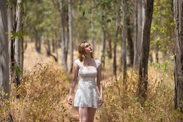 Young woman, beautiful, blonde, wearing a floral dress, relaxed and calm, walking among the trees, in connection with nature and ecology, in an outdoor park. Concept of beauty, youth, millennial.