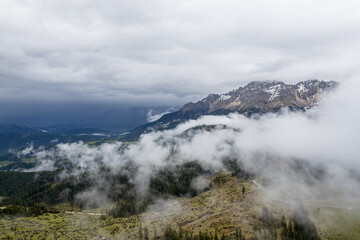 Clouds surround rocky peaks of the Dolomites mountains in Italy on a moody day.