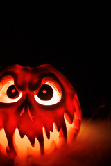 Fototapeta premium Glowing carved pumpkin with smoke flowing out of its mouth, symbol of fear and Halloween on black backdrop.