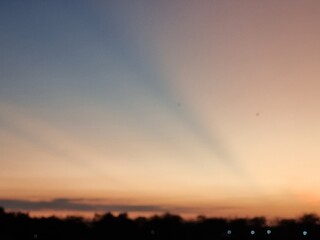Blurred colorful evening sunset sky with soft gradient and sun rays above dark horizon