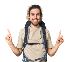 Young Caucasian hiker with backpack indicates with both fore fingers up showing a blank space.