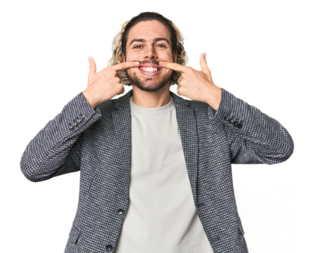 Young businessman in casual blazer smiles, pointing fingers at mouth.