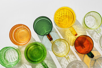 Colorful glowing glass cups on white background, casting artistic light reflections and shadows in natural sunlight. Summer drink concept, minimal trend pattern of transparent glasses, caustics