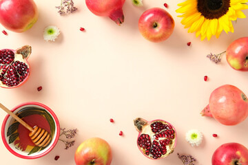Flat lay of apples, pomegranates, honey, and flowers on peach background. Happy Rosh Hashanah greeting card template.