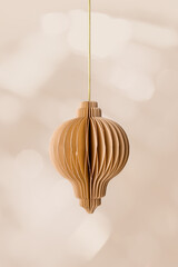 Brown paper Christmas ornament, neutral color New year flashlight hanging on gold string, on light beige bokeh background win sun glare. Christmas bauble, winter holiday decor, honeycomb scandi style.
