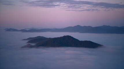 Fototapeta premium Aerial view of mountainous terrain shrouded in dense fog at dawn or dusk,